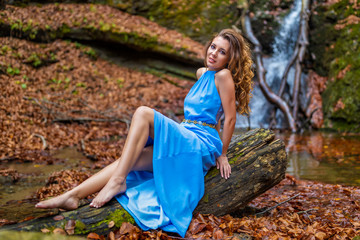 A beautiful woman in blue dress near a waterfall in autumn day
