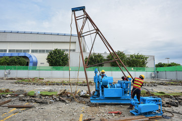 Construction workers assembly rig and machine for soil investigation works at construction site.