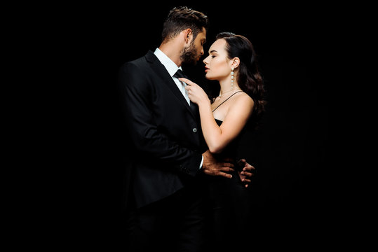 attractive woman in dress hugging boyfriend in suit isolated on black