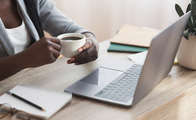 Afro businesswoman having coffee while working on laptop in office