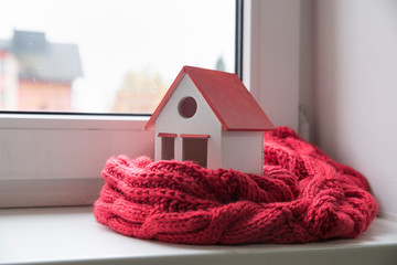 house in winter - heating system concept and cold snowy weather with model of a house wearing a...