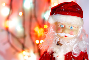 Toy, figurine, Santa Claus. Toy Santa Claus on the background of garland lights. Face, parts of the body of Santa Claus. New Year's toy in macro. The suit is red, a large gray white beard.
