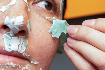 removing a green cosmetic clay mask from the attractive girl face with freckles