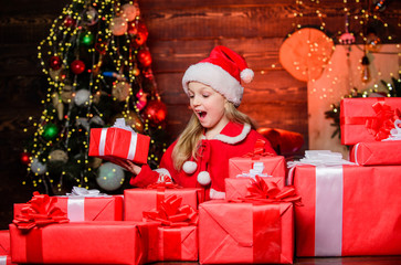 Santa brought me gifts. Child happy excited girl find gifts near christmas tree. Happiness and joy. Merry christmas. Happy childhood concept. Kid wear santa hat hold wrapped christmas gift box