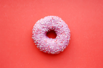Donut with pink icing and colorful confetti, on a red background