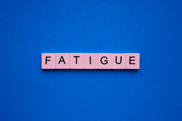 Fatigue word wooden cubes on blue background