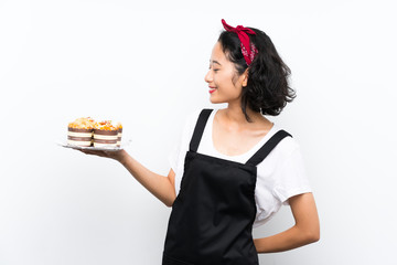 Young asian girl holding lots of muffin cake over isolated white background with happy expression