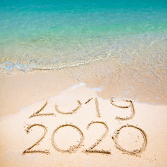 Happy New Year 2020, lettering on the beach with wave and clear blue sea. Numbers 2020 year on the...