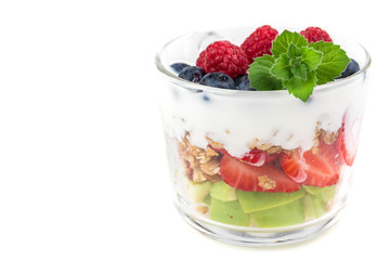 Portion cup with yogurt and muesli. Pieces of fruit are laid in layers, spilled with soys. Granola is decorated with mint leaf and fresh raspberry. White background. Copyspace