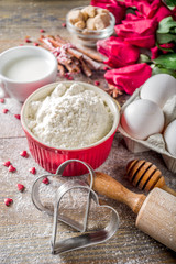 Valentine day baking background. Ingredients for cooking Valentine's heart cookies. Flour, eggs, sugar, spices on wooden background with red flower roses. Top view copy space.
