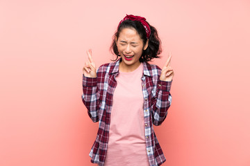 Asian young woman over isolated pink background with fingers crossing