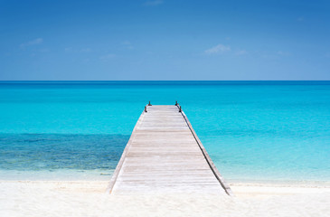 Fototapeta na wymiar Wooden bridge or pier on tropical white sand beach with clear blue sea and sky on sunny day. Boardwalk into the ocean and turquoise water. Summer holidays background with copy space. Kuramathi Island.