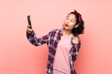 Asian young woman over isolated pink background making a selfie