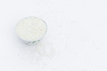 Milled rice in a cup and milled rice spread on a white ground