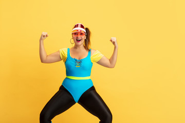 Young caucasian plus size female model's training on yellow background. Copyspace. Concept of sport, healthy lifestyle, body positive, fashion, style. Stylish woman posing like superhero, girl power.