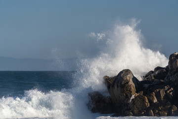 Large wave crashing onto jagged rocks in Monterey Bay, California