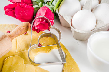 Valentine day baking background. Ingredients for cooking Valentine's heart cookies. Flour, eggs, sugar, spices on wooden background with red flower roses. Top view copy space.