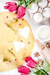 Valentine day baking background. Ingredients for cooking Valentine's heart cookies. Flour, eggs, sugar, spices on wooden background with red flower roses. Top view copy space.