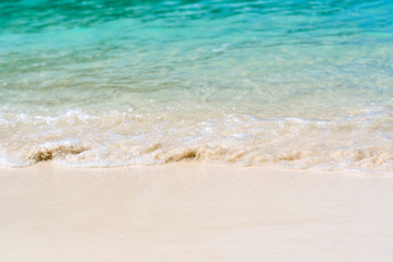 Soft wave splash on the sandy beach summer tropical concept. Close up of white sea foams and bubbles hitting the clean white sand beach with blurred of clear blue sea background, copy space.