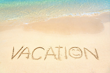 Vacation, lettering on golden sand  beach with wave and clear blue sea. Sun or smile face drawing and message handwritten in sand on beautiful beach. Holiday background sign concept, copy space.