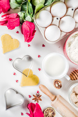 Valentine day baking background. Ingredients for cooking Valentine's heart cookies. Flour, eggs, sugar, spices on wooden background with red flower roses. Top view copy space.