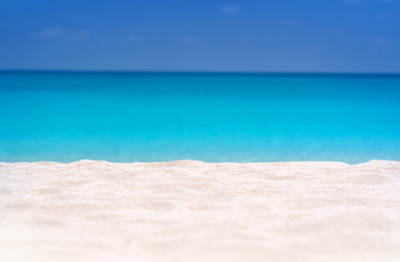 Close up of tropical sand with blurred sea and sky background, summer day. Sandy beach with blurry blue ocean copy space for product.