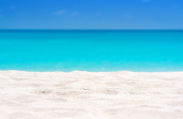 Fototapeta na wymiar Close up of tropical sand with blurred sea and sky background, summer day. Sandy beach with blurry blue ocean copy space for product.