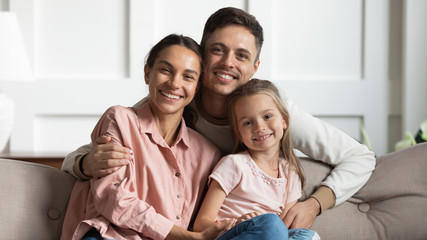 Beautiful young parents with small daughter sit on sofa, portrait