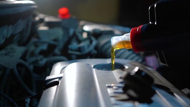 Engine oil change. Fresh engine oil pouring from the canister into the automobile engine. Proper car care background.