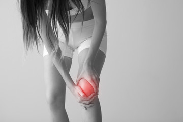 Young woman suffering from pain in knee on light background - obrazy, fototapety, plakaty