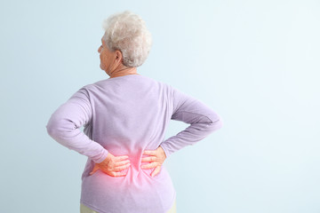 Senior woman suffering from pain in back against light background