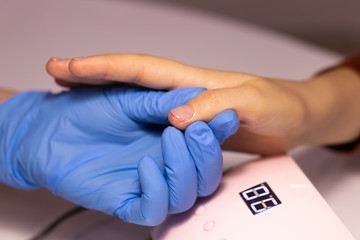 A hand in a blue glove holds the thumb of a client whose skin and nail are smeared with oil.