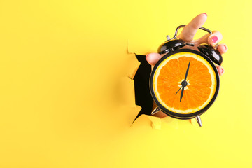 Female hand with alarm clock visible through hole in torn color paper