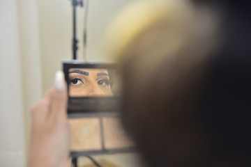 woman looking at herself in the mirror, reflection of a woman's eyes applying makeup in a small compact mirror, beauty routine and self-care moment, shallow depth of field
