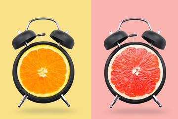 Different citrus fruits in alarm clocks on color background