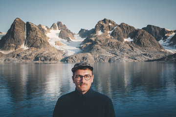 Young Traveler Man with hat relaxing and smiling with serene view mountains and lake landscape Travel Lifestyle hiking concept summer vacations outdoor. Greenland mountains with Glacier. © Mathias