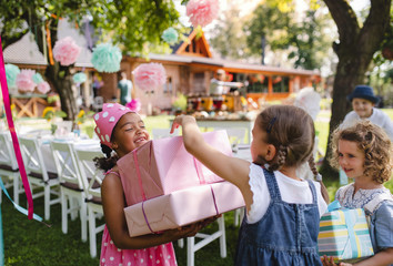 Obraz premium Portrait of small girl with friends and presents outdoors in garden in summer.
