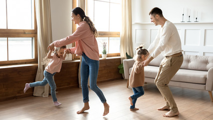 Happy parents and kids daughters dancing spinning together at home