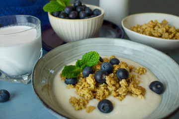 Food photography of a ceramic bowl with yogurt, granola cereal and blueberries on a blue background.