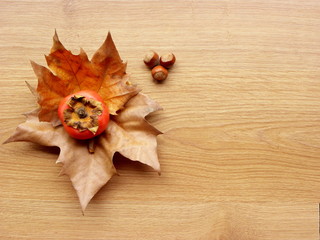 persimmons, hazelnuts and autumn leaves on wooden background