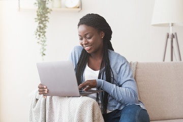 Young black woman working with laptop on sofa at home