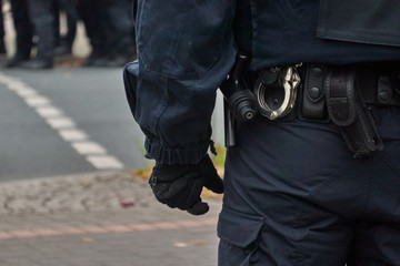 Belt of a policeman in black uniform in action, with handcuffs, baton and belt bag.