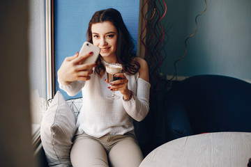 A girl is sitting near the window. She is alone in cafe. She has a dessert.