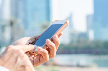 close up business man using hand typing smartphones and touch screen working search with app devices outdoor in city with sunrise and building background. 5G technology connecting the world.