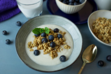 Food photography of a ceramic bowl with yogurt, granola cereal and blueberries on a blue background.