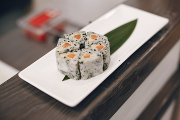 There is a close-up of sushi put on plate. Sushi are with salmon. The background is dark.