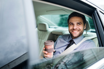 Businessman with coffee sitting on back seat in car.