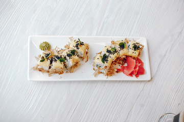 Sushi are on wooden table. Sushi are on white plate. Sushi served with wasabi and ginger.