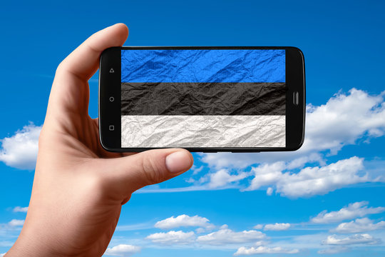 Estonia flag on the phone screen. Smartphone in hand shows a flag on a background of the sky with clouds.
