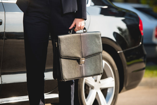 cropped view of ambassador standing near car with briefcase